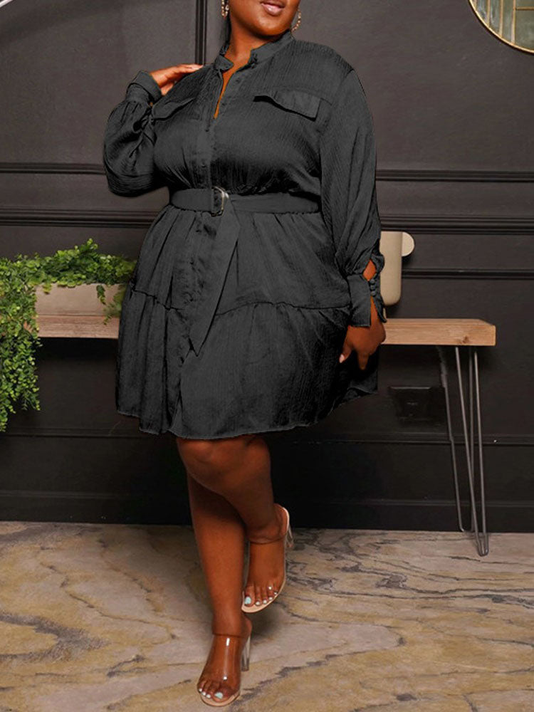 Woman wearing a black shirt dress with a belted waist and tiered hem, front view.