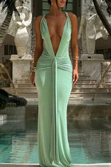 Woman wearing a long, light green shimmering dress with a deep V-neck and gathered waist, standing by a pool.