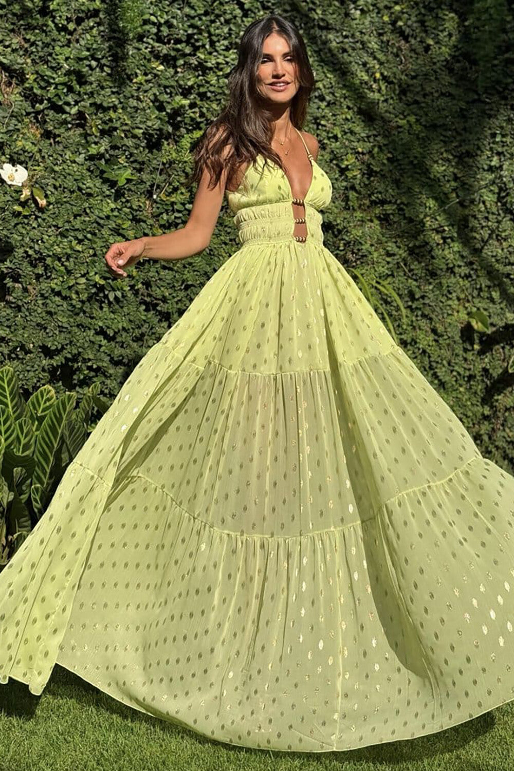 Woman in a flowing lime green maxi dress with gold polka dots, twirling in a garden setting.