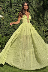 Woman in a flowing lime green maxi dress with gold polka dots, twirling in a garden setting.