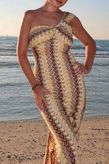 Woman wearing a yellow and brown patterned one-shoulder knit dress on a beach.