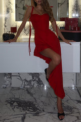 Woman wearing a red asymmetrical hemline dress with ruffle detailing and tie straps, leaning against a vanity in a modern bathroom.