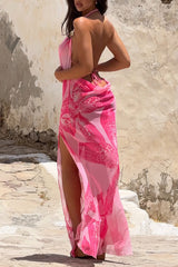 Woman wearing a pink floral maxi dress with a thigh-high slit, posing against a textured wall.