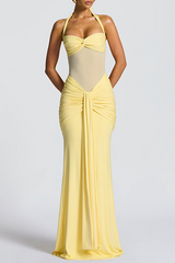 Model posing in a yellow floor-length dress with a draped skirt and halter neckline.