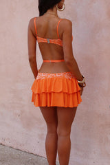 Back view of a woman wearing an orange lace and fabric set with a sweetheart neckline and tiered skirt.