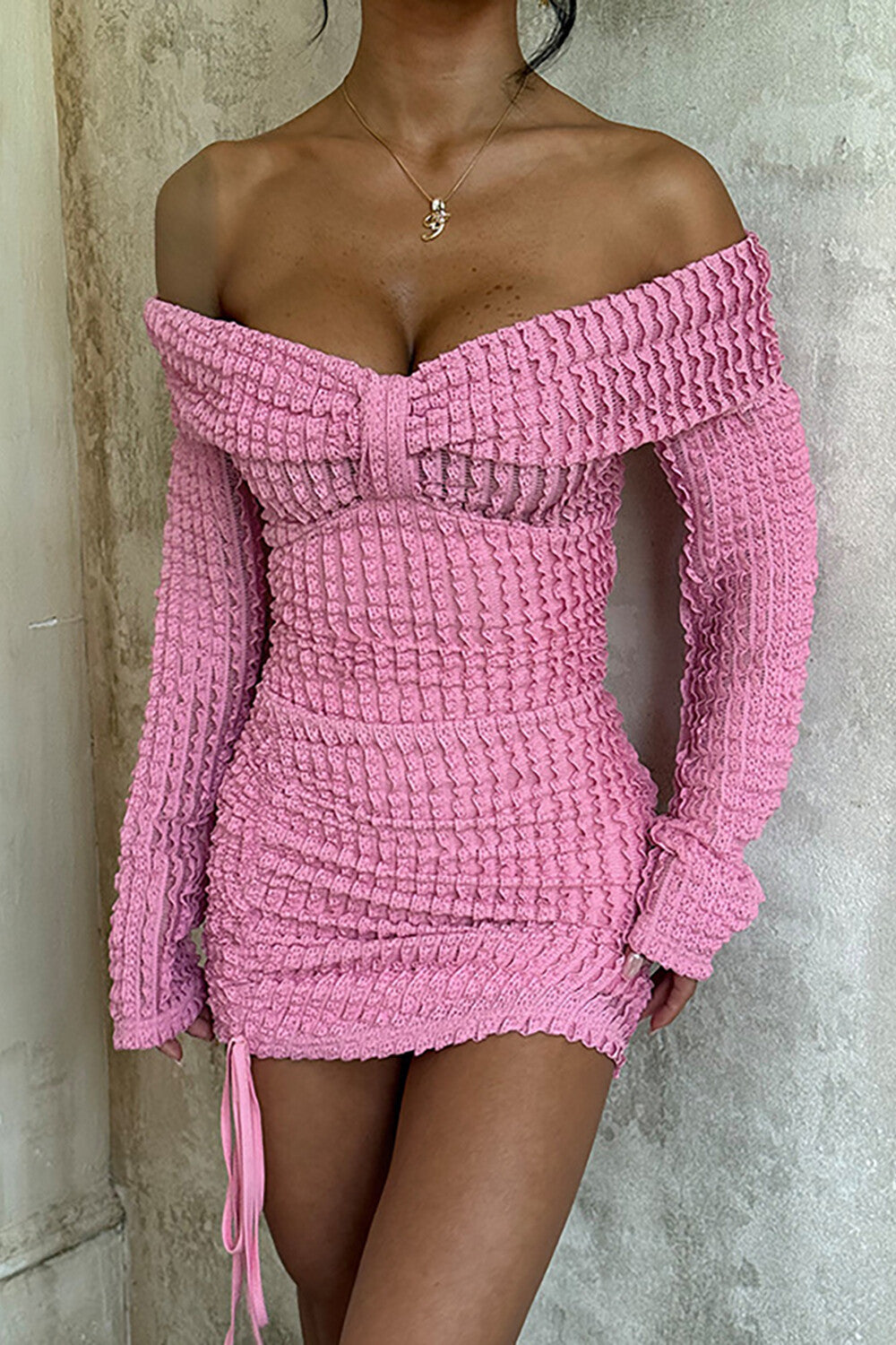 Woman wearing a pink off-the-shoulder ruched knit mini dress with long sleeves and a drawstring hem.
