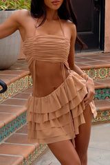 Woman wearing a tan ruched halter crop top and a tiered ruffle mini skirt, standing on outdoor stairs.