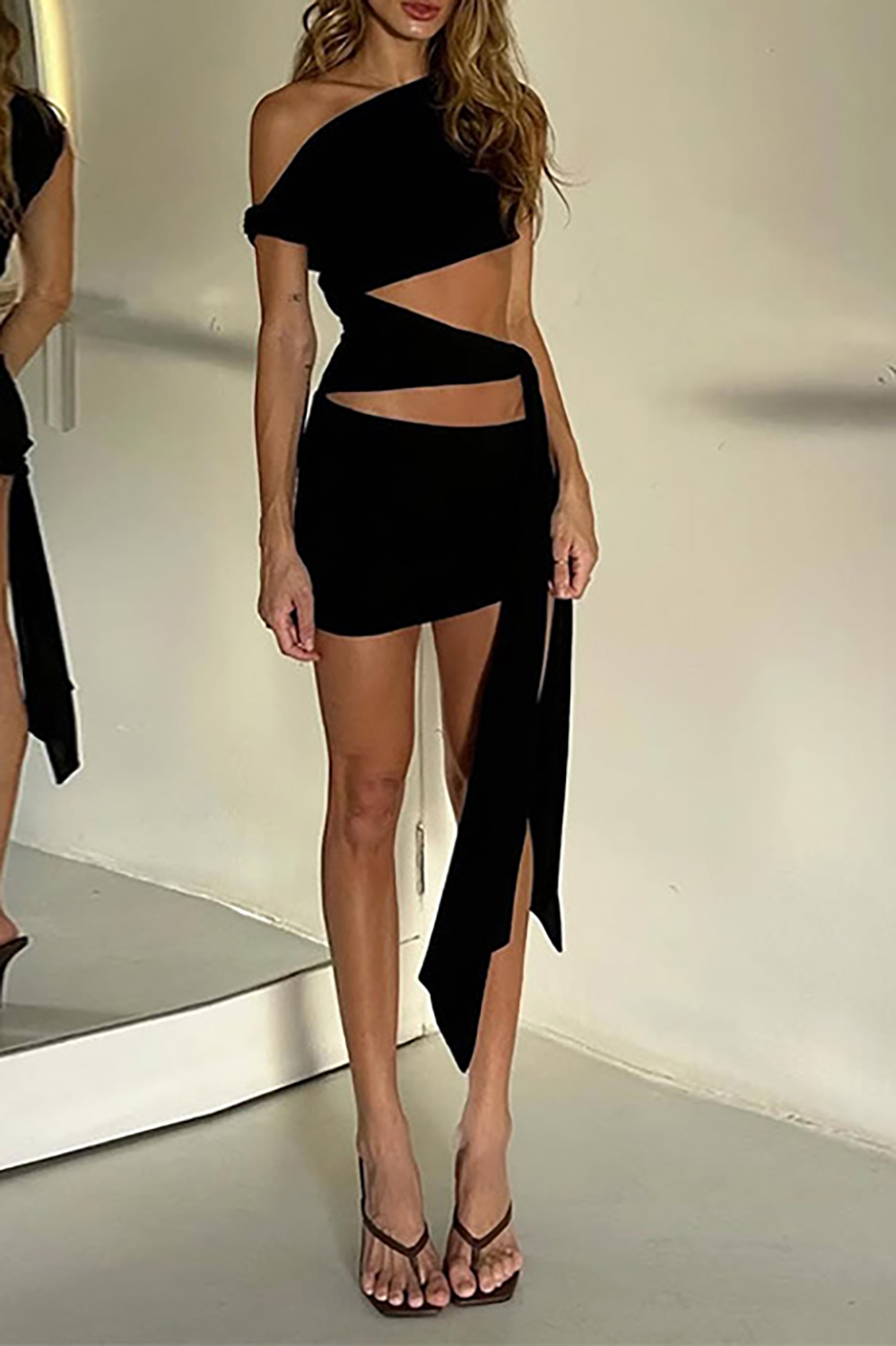 front view of a black one-shoulder asymmetrical cut-out mini dress with a waist tie
