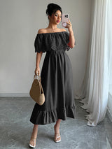 Woman taking a mirror selfie wearing a black off-the-shoulder maxi dress with lace bodice and ruffled hem, holding a straw bag