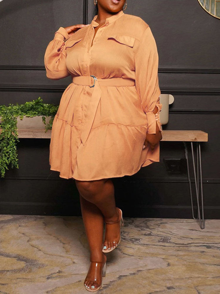 Back view of a plus-size woman wearing a long-sleeved, collared, belted mini dress with a tiered skirt in a peachy-orange color.