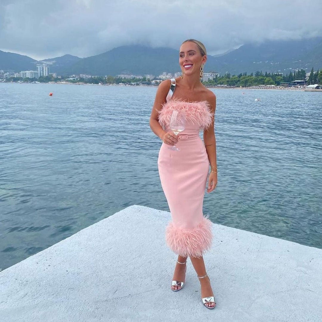 woman in a pale pink strapless midi dress with feather trim, standing by the water
