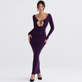 Woman wearing a long purple dress with a plunging neckline and long sleeves, standing against a white background.
