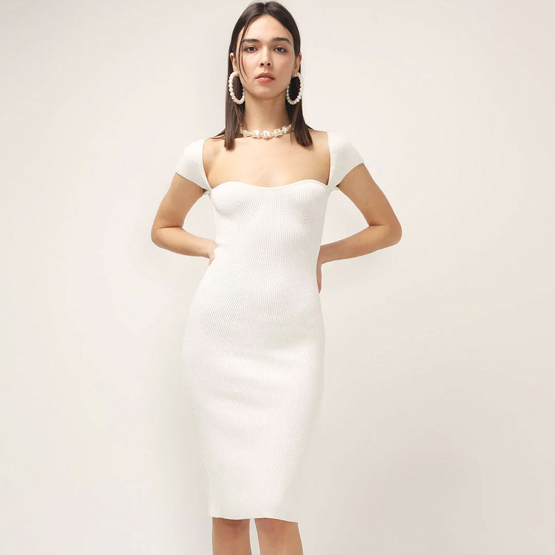 Woman wearing a white ribbed knit dress with short sleeves and a square neckline, accessorized with pearl jewelry.