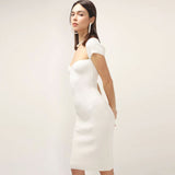 Side view of a woman in a white ribbed knit sheath dress with short sleeves and a square neckline.