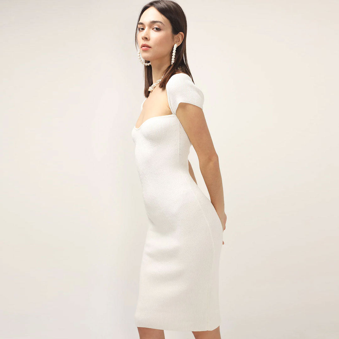 Side view of a woman in a white ribbed knit sheath dress with short sleeves and a square neckline.