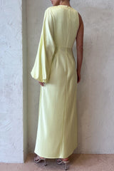 Back view of a woman in a pale yellow satin one-shoulder maxi dress, showing the sleek silhouette and the long asymmetrical sleeve.
