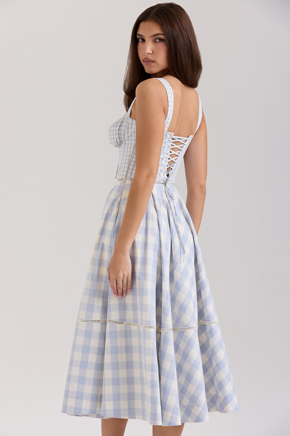 Back view of a woman wearing a blue and white gingham check midi dress with corset lacing.