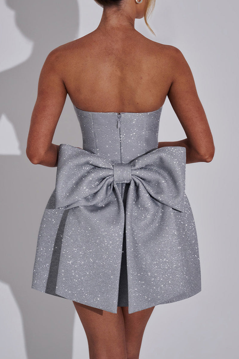 Detail shot of the back of a silver glitter strapless dress, highlighting the voluminous bow and the fitted bodice.