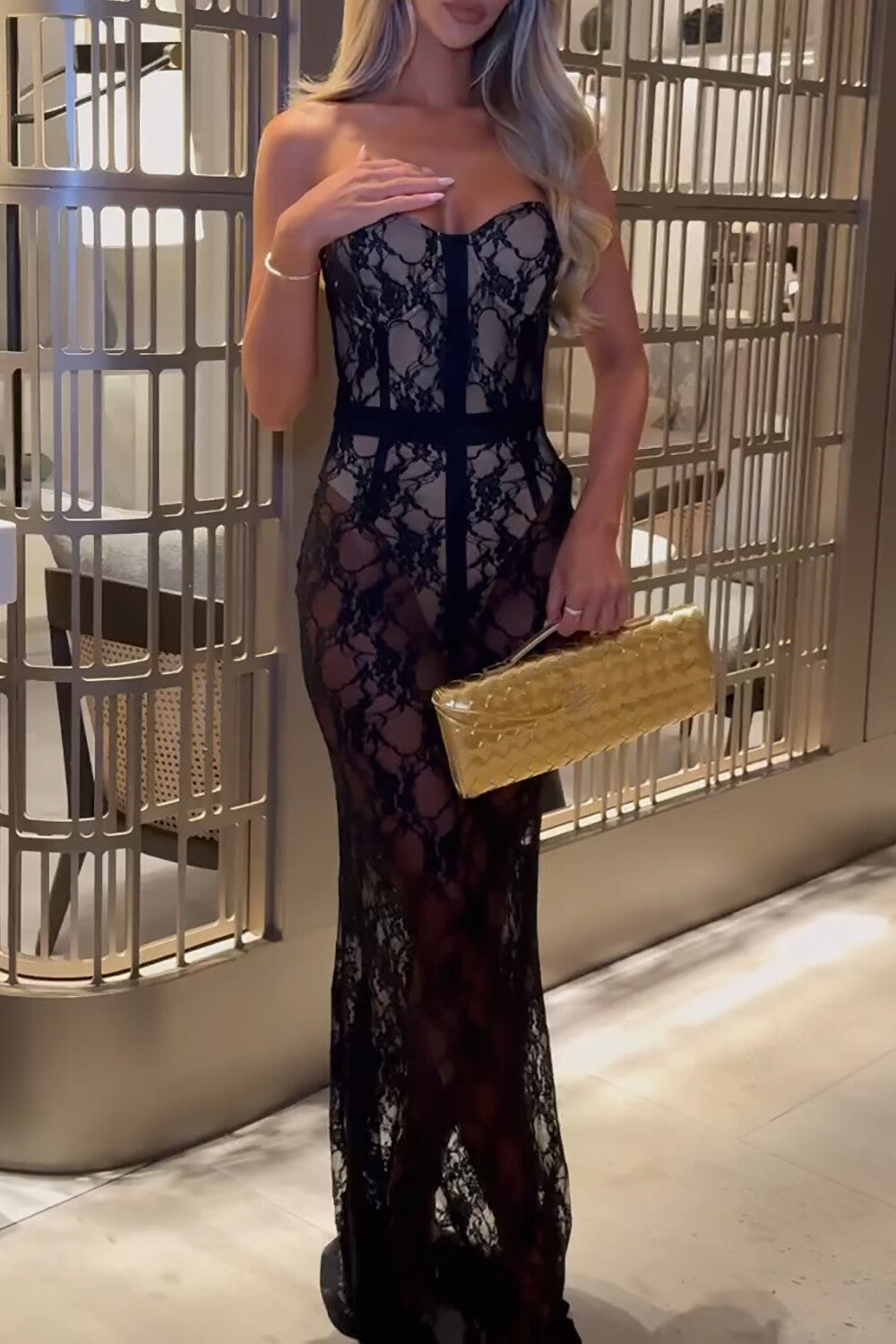 Full-body shot of a woman in a black strapless lace gown posing in an elegant interior setting.