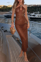 Woman wearing a long, sheer, brown, embellished dress with a halter neckline, standing on a yacht.