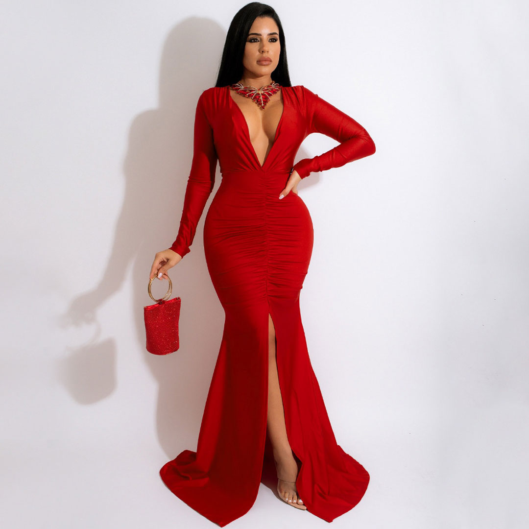 woman wearing a red long-sleeve evening gown with a deep V-neckline and high slit, holding a red beaded clutch