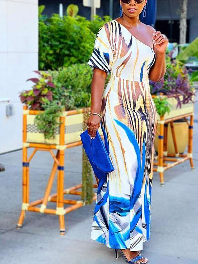 Woman wearing a one-shoulder maxi dress with an abstract print, holding a blue clutch, outdoors.