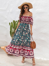 Woman wearing a teal and red floral off-the-shoulder maxi dress, straw hat, sunglasses, and a round straw bag.