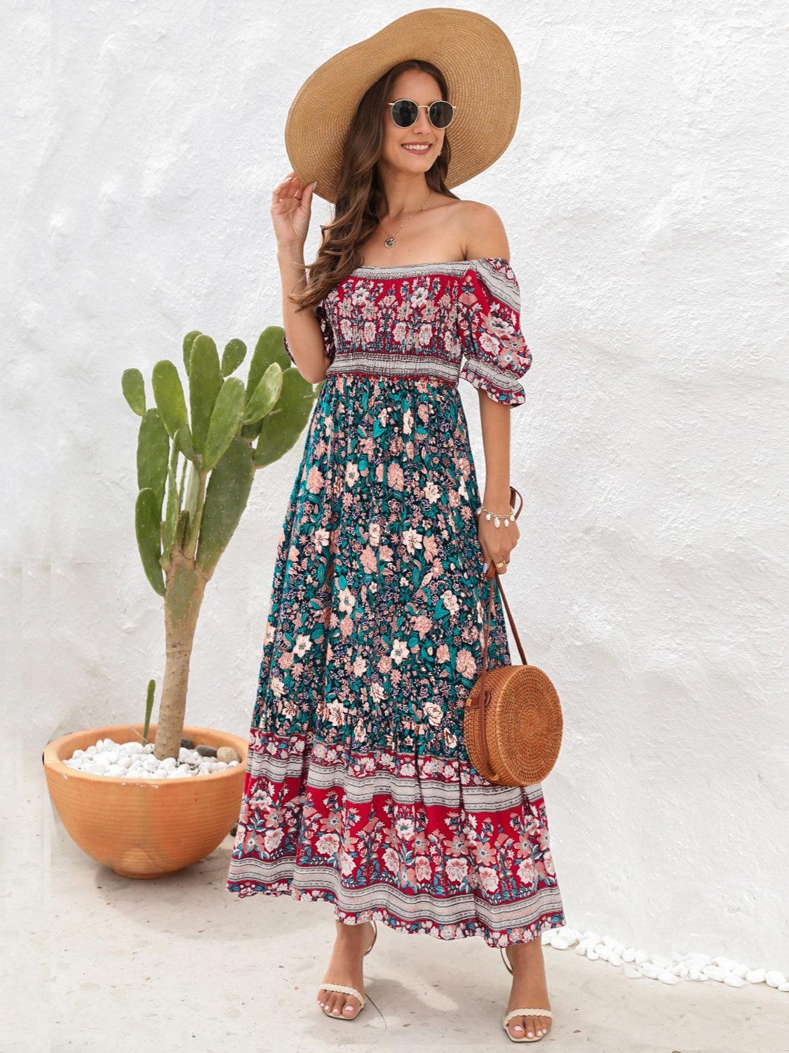Woman in a teal and red floral off-the-shoulder maxi dress, straw hat, sunglasses, and a round straw bag, smiling.