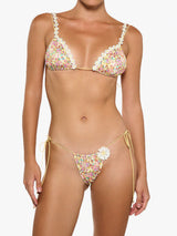 Woman wearing a floral print triangle bikini top with daisy embellishments and string ties, and a matching floral print string bikini bottom with a daisy embellishment.