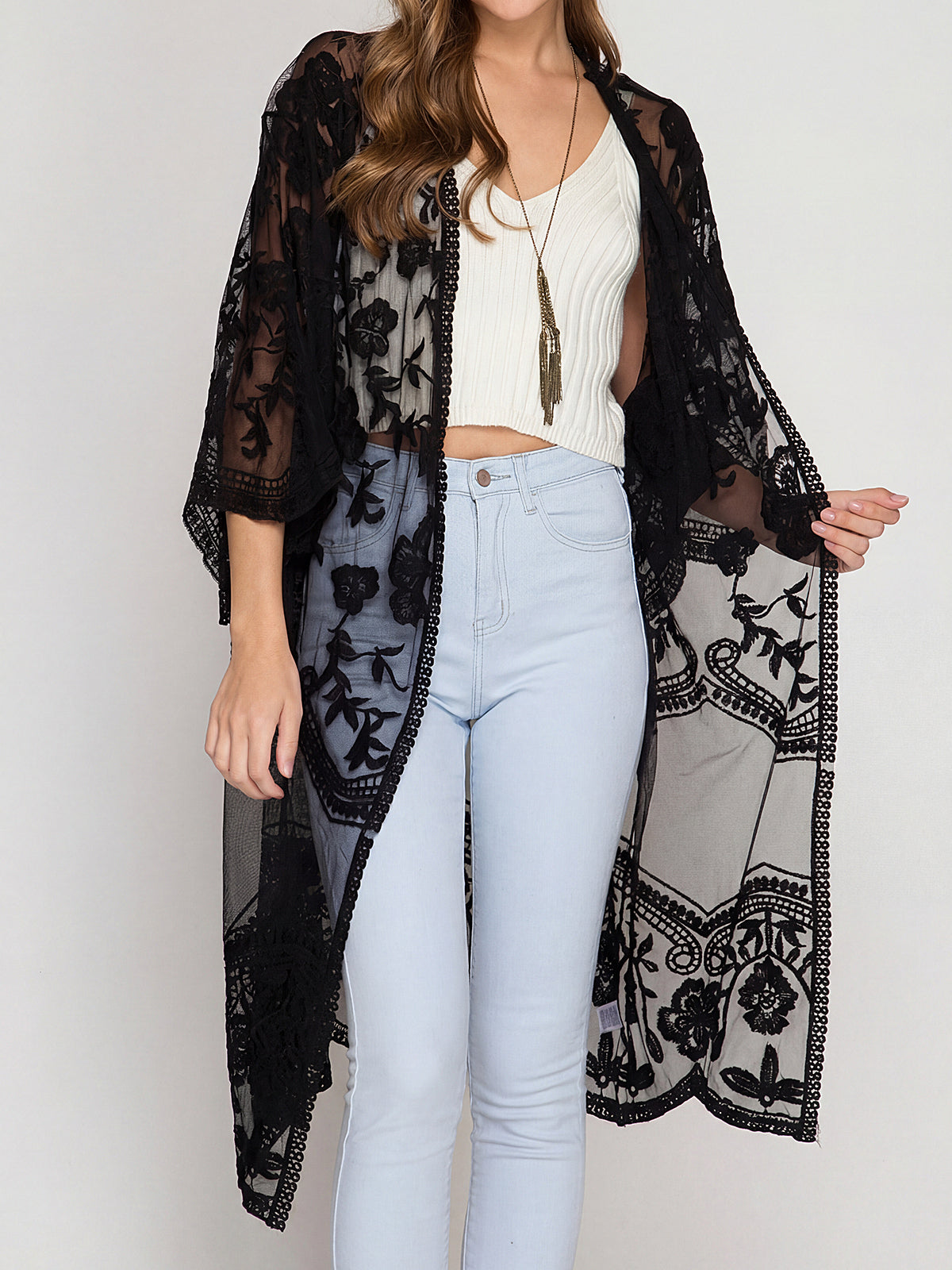 woman wearing a black lace kimono over a white crop top and light blue jeans