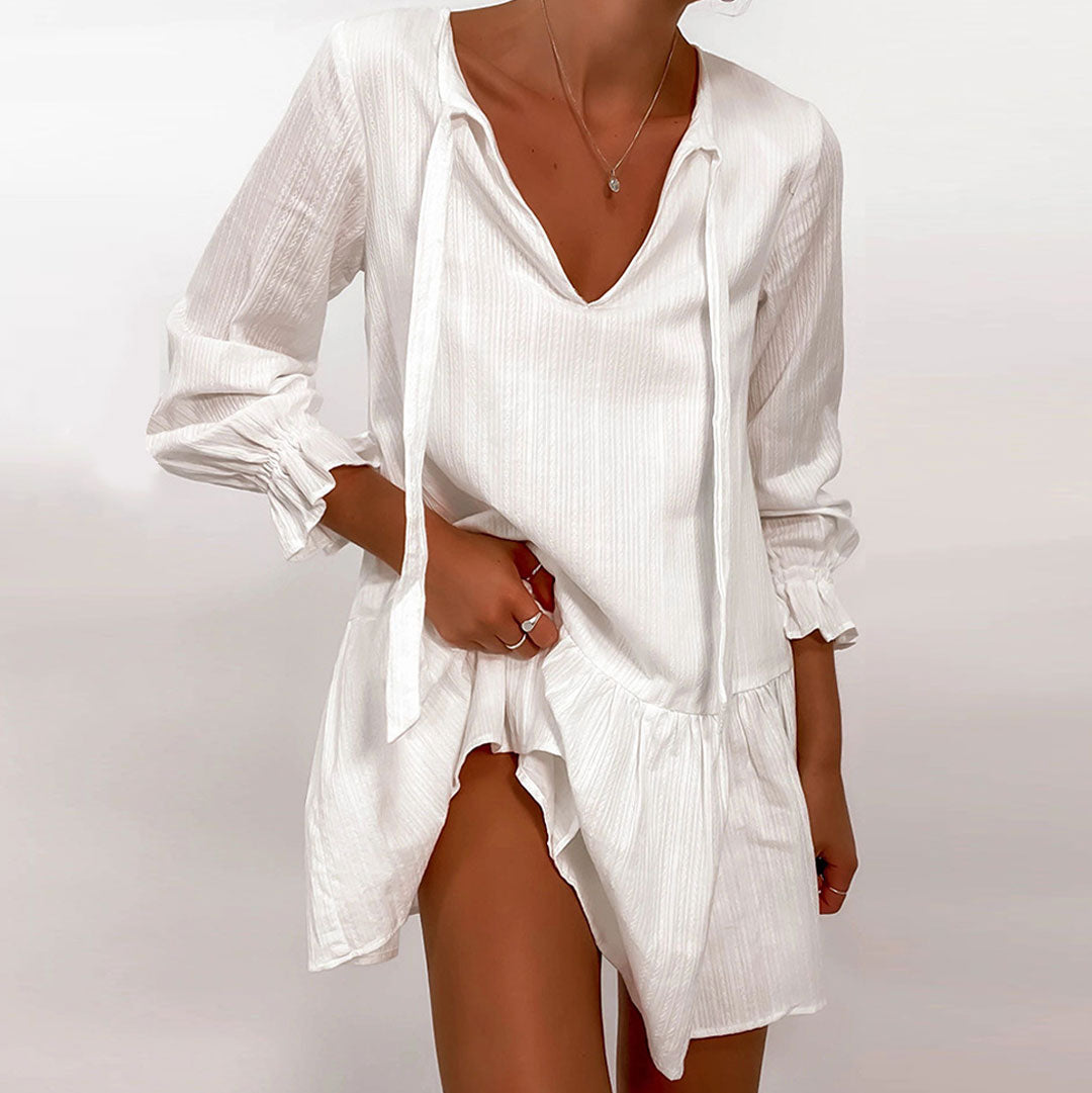 Woman wearing a white V-neck mini dress with tie detail and ruffled cuffs