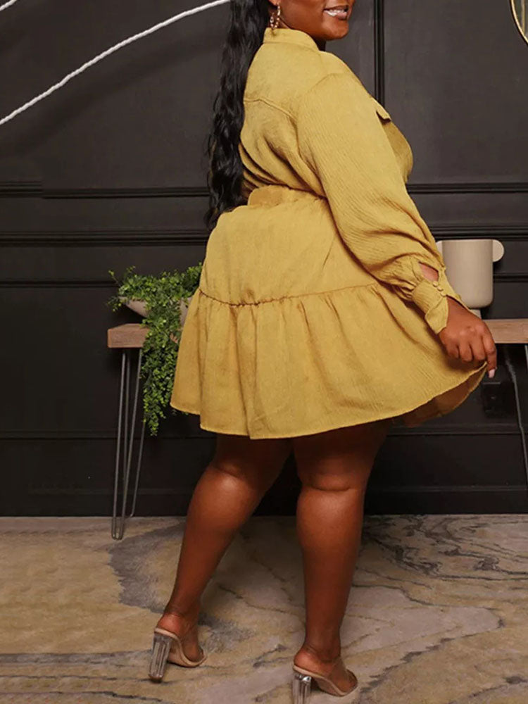 Back view of a woman wearing a mustard yellow shirt dress with a belted waist and tiered hem.