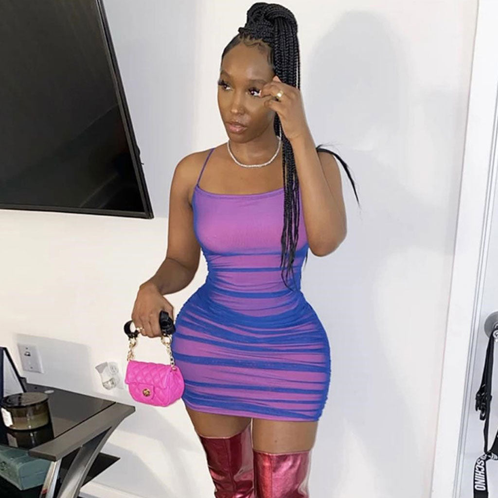 Woman in a pink and blue ruched mesh bodycon dress holding a pink handbag and wearing red boots