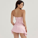 Back view of a woman in a light pink strapless satin mini dress, showing the zipper closure.
