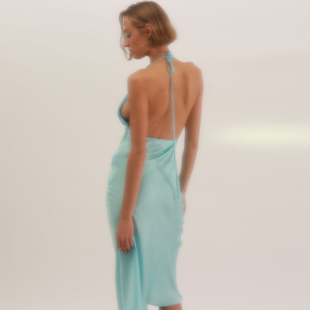 Rear view of a woman in a light blue satin slip dress with a low open back and halter tie closure.