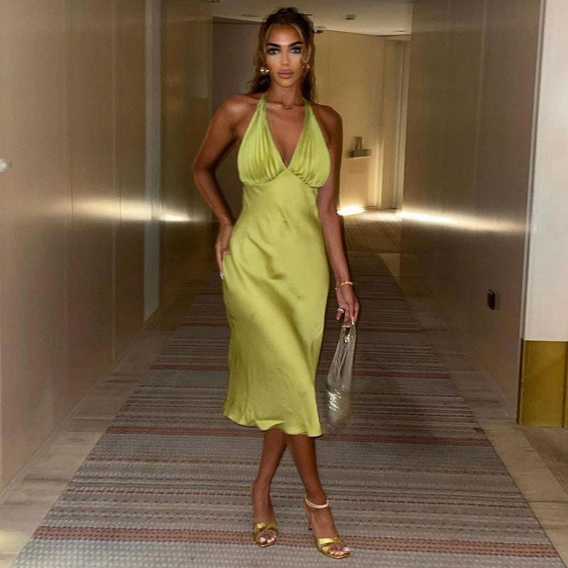 Woman wearing a lime green satin halter midi dress, standing in a hotel hallway and facing the camera.