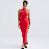 Woman wearing a floor-length red satin halter dress with a large bow at the back, standing against a white background.