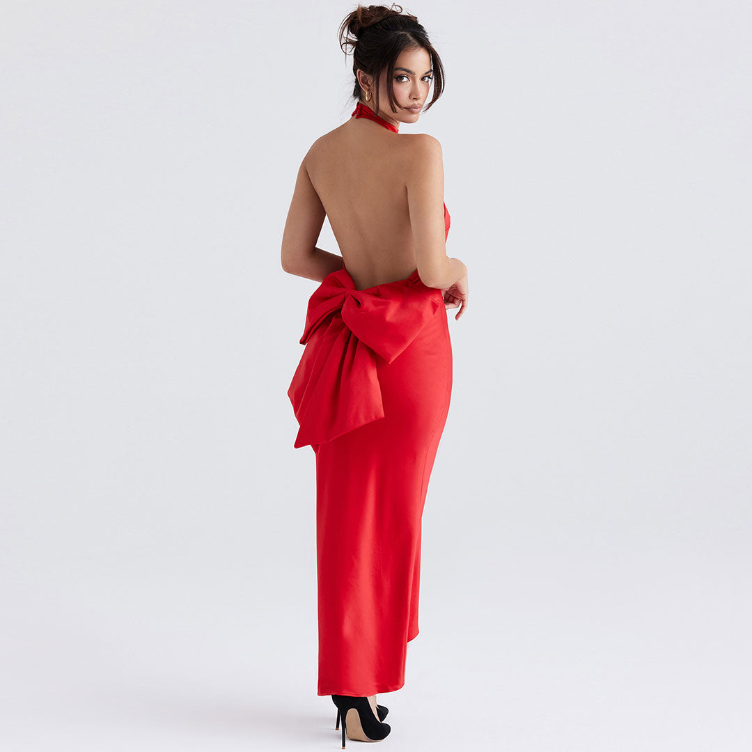 Back view of a woman in a floor-length red satin halter dress, showcasing the open back and prominent bow.