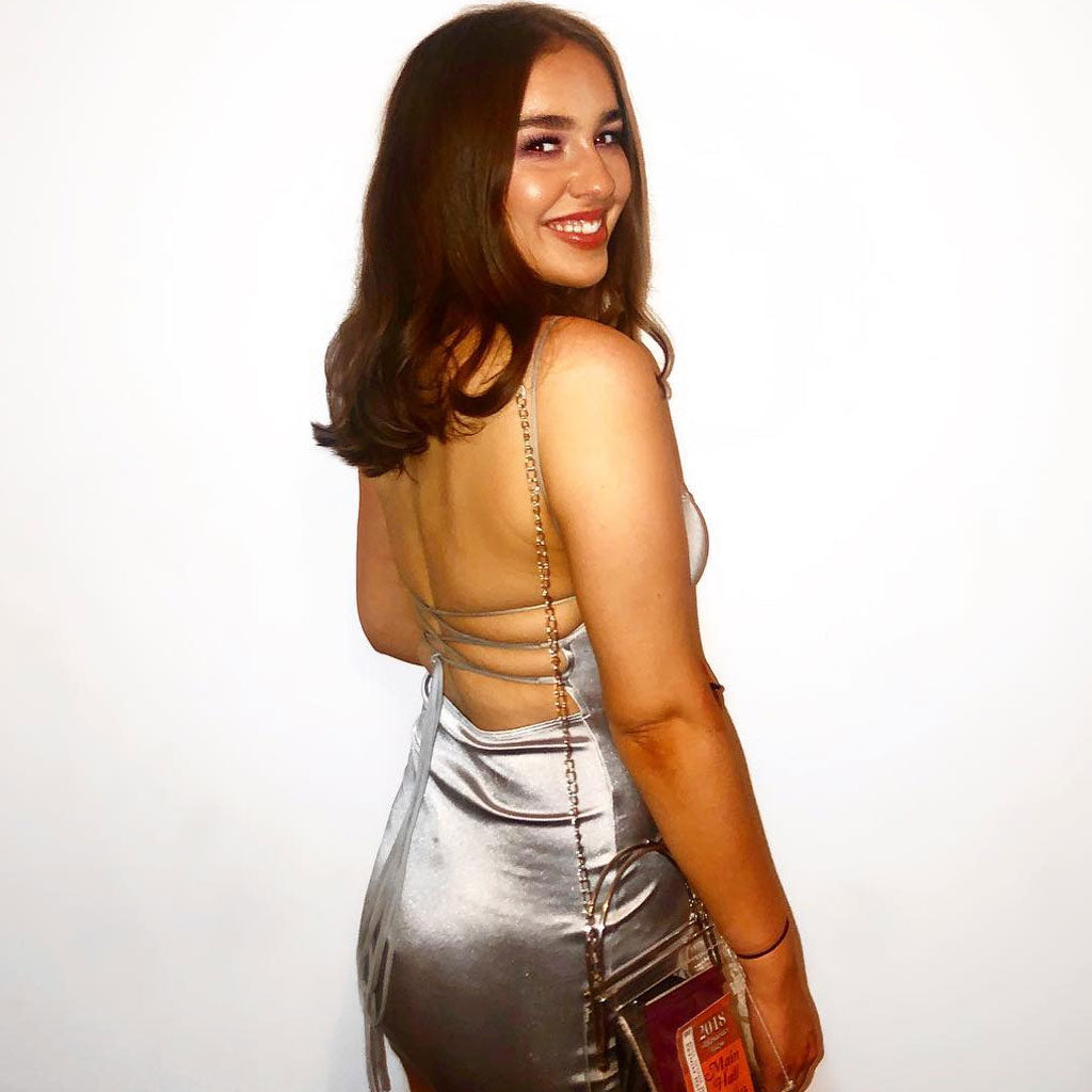 Woman in a silver satin mini dress with an open back and criss-cross straps.