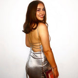Woman in a silver satin mini dress with an open back and criss-cross straps.