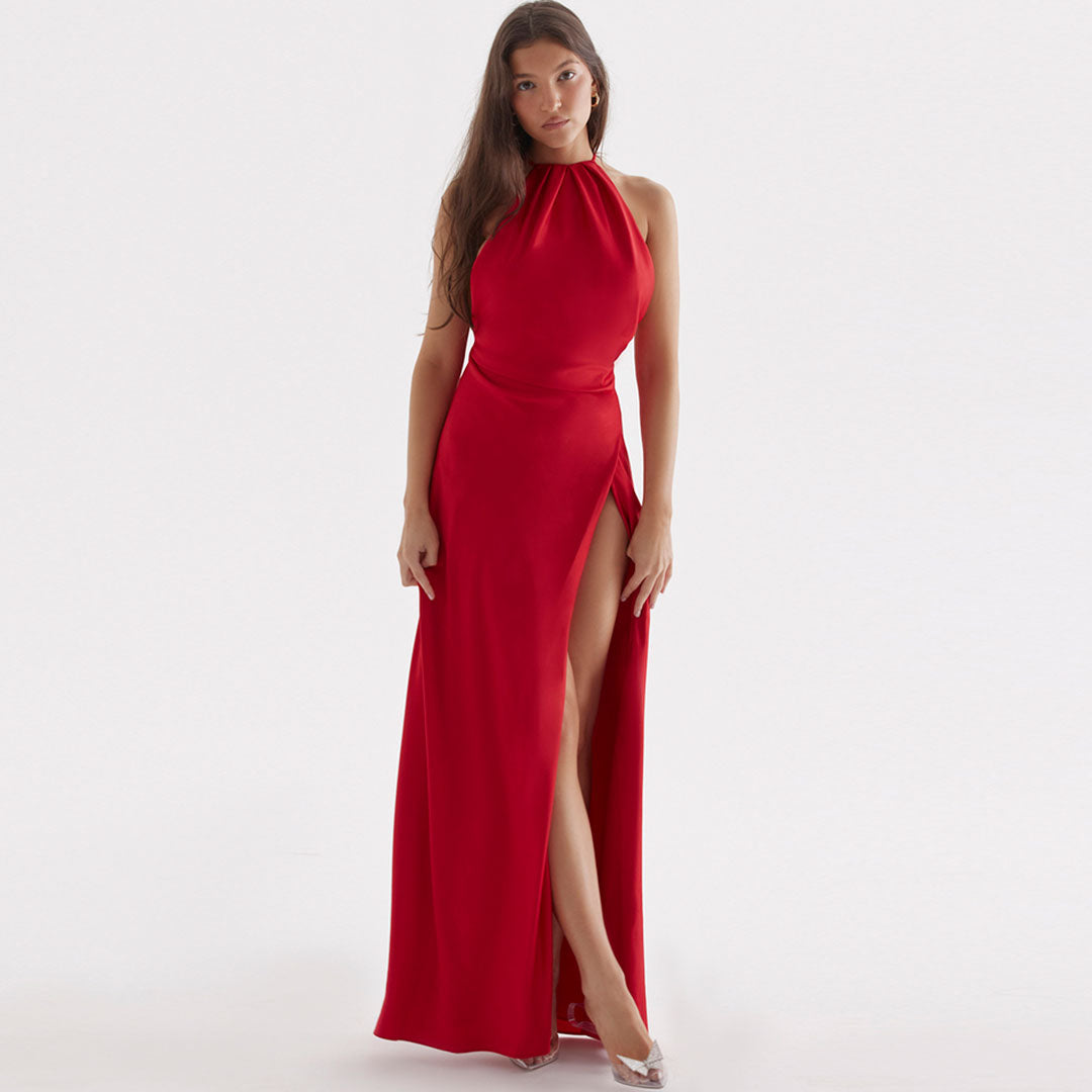 Woman wearing a long red satin dress with a high slit and halter neckline, standing against a white background.