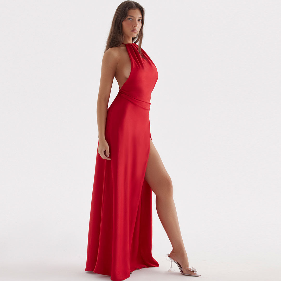 Side view of a woman in a long red satin dress with a high slit and halter neckline, showcasing the dress's drape.