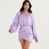Woman posing in a lavender satin mini dress with long balloon sleeves and ruched detailing.