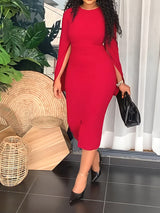 Woman wearing a red sheath dress with cape sleeves and a slit hem.