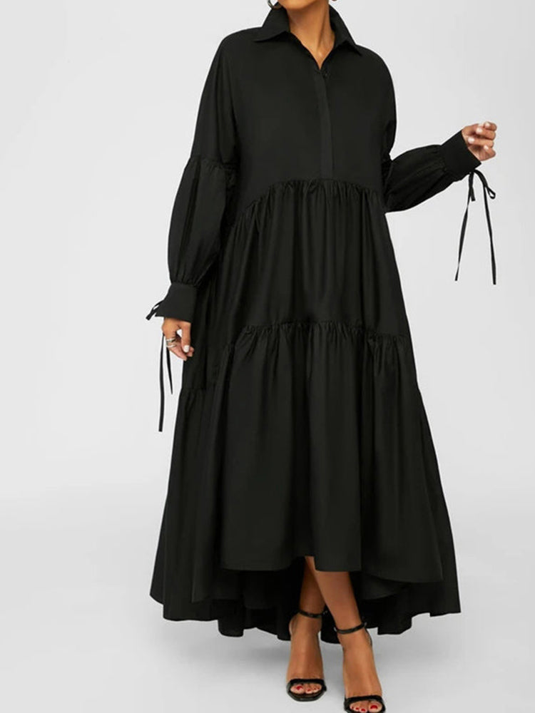 Front view of a woman wearing a black tiered maxi dress with balloon sleeves featuring tie cuffs, standing indoors.