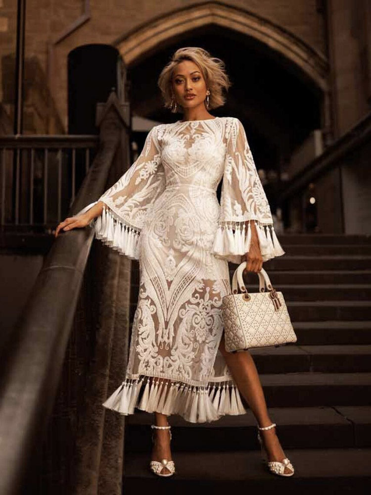 woman posing on stairs in a white lace dress with bell sleeves and fringe detail, holding a white handbag
