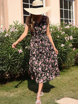 Woman in a black floral print midi dress and straw hat, posing outdoors