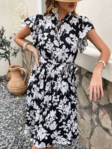 Close-up of a woman in a black and white floral print midi dress, showcasing the ruffled sleeves and belted waist.