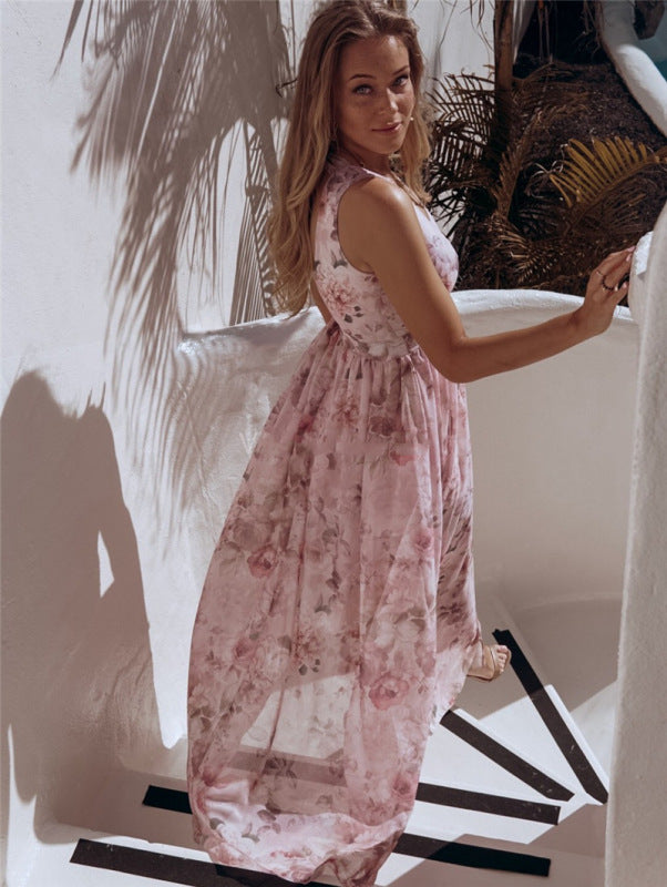 Woman wearing a pink floral print maxi dress with a high slit, turning on white stairs with palm leaf shadows.