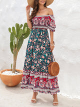 Woman wearing a floral print off-the-shoulder maxi dress with puff sleeves, a tiered skirt, and a straw hat, holding a straw bag.